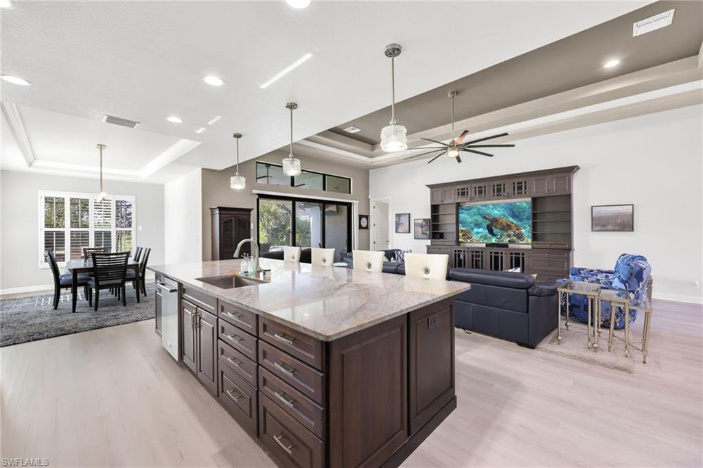 Kitchen featuring dark brown cabinets, light stone countertops, light wood-type flooring, hanging light fixtures, and a kitchen island with sink