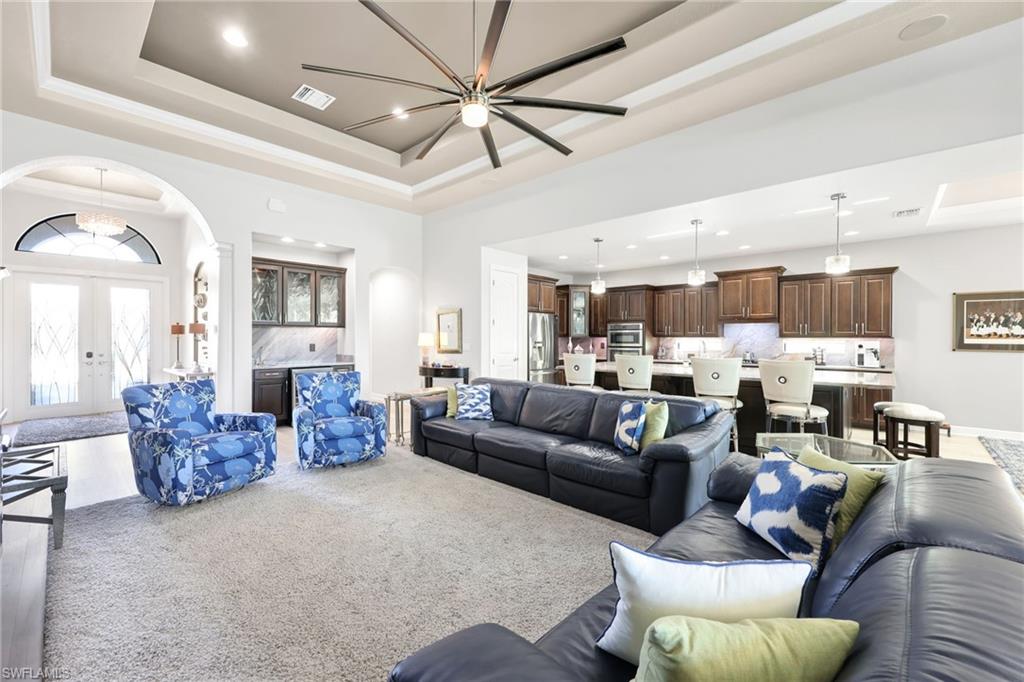 Living area featuring arched walkways, a raised ceiling, recessed lighting, light carpet, and french doors