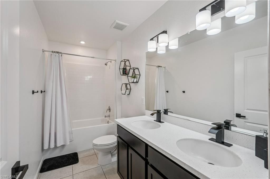 Full bath with shower / bath combo, double vanity, and light tile patterned floors