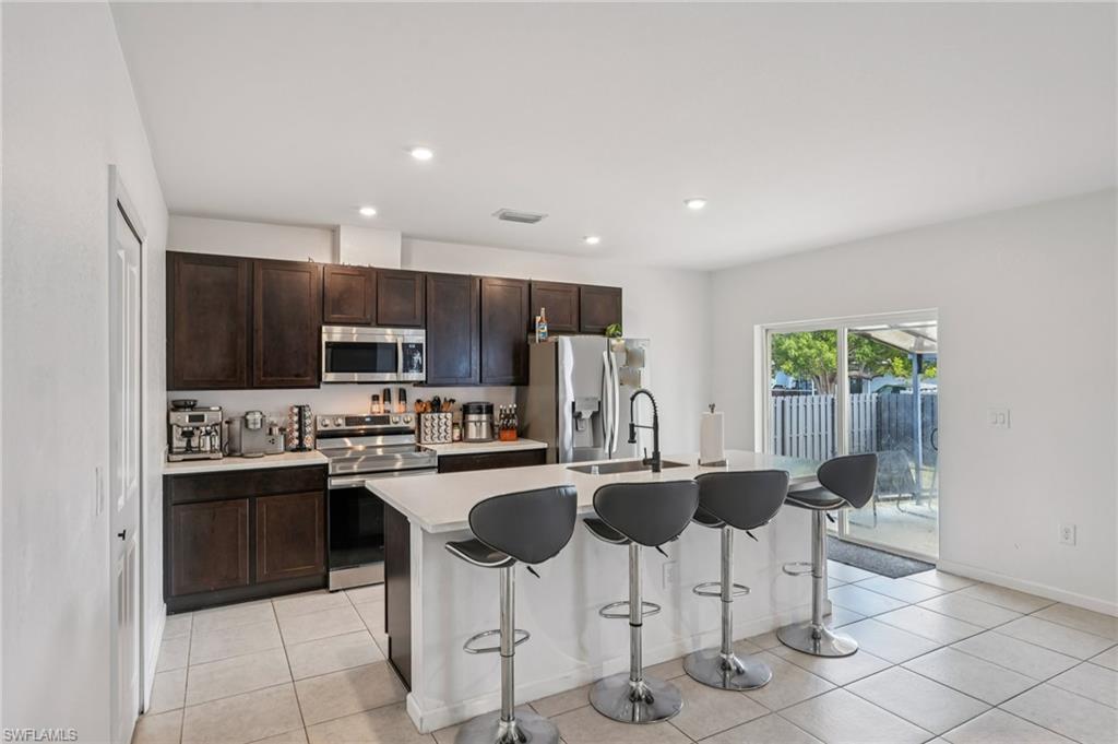 Kitchen with stainless steel appliances, a center island with sink, a breakfast bar area, dark brown cabinets, and light tile patterned floors