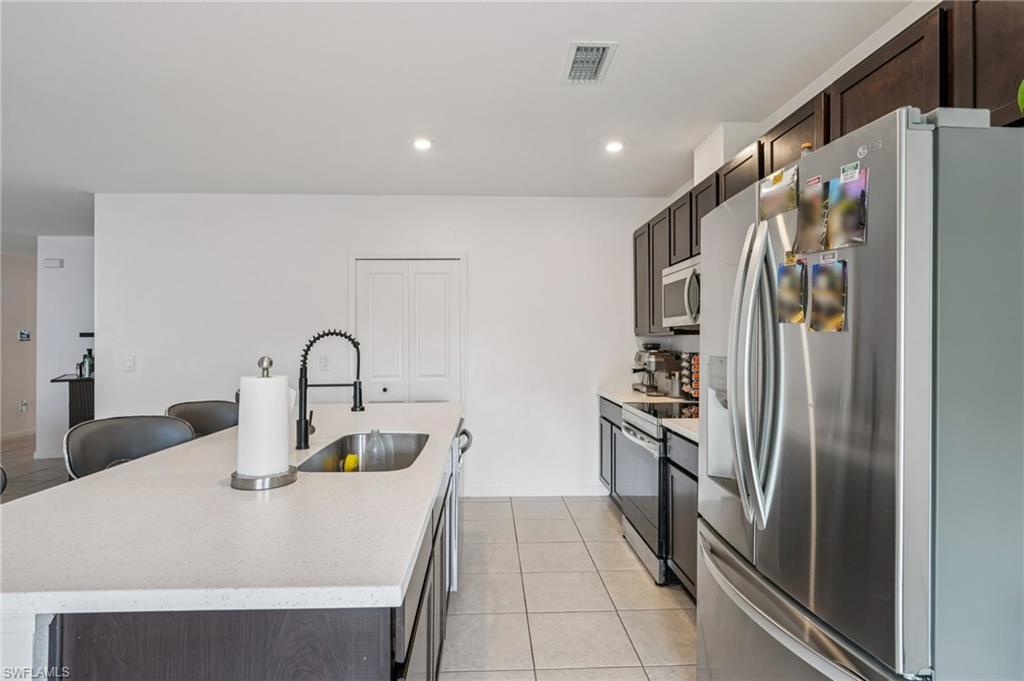 Kitchen featuring stainless steel appliances, a kitchen island with sink, light tile patterned floors, recessed lighting, and dark brown cabinets
