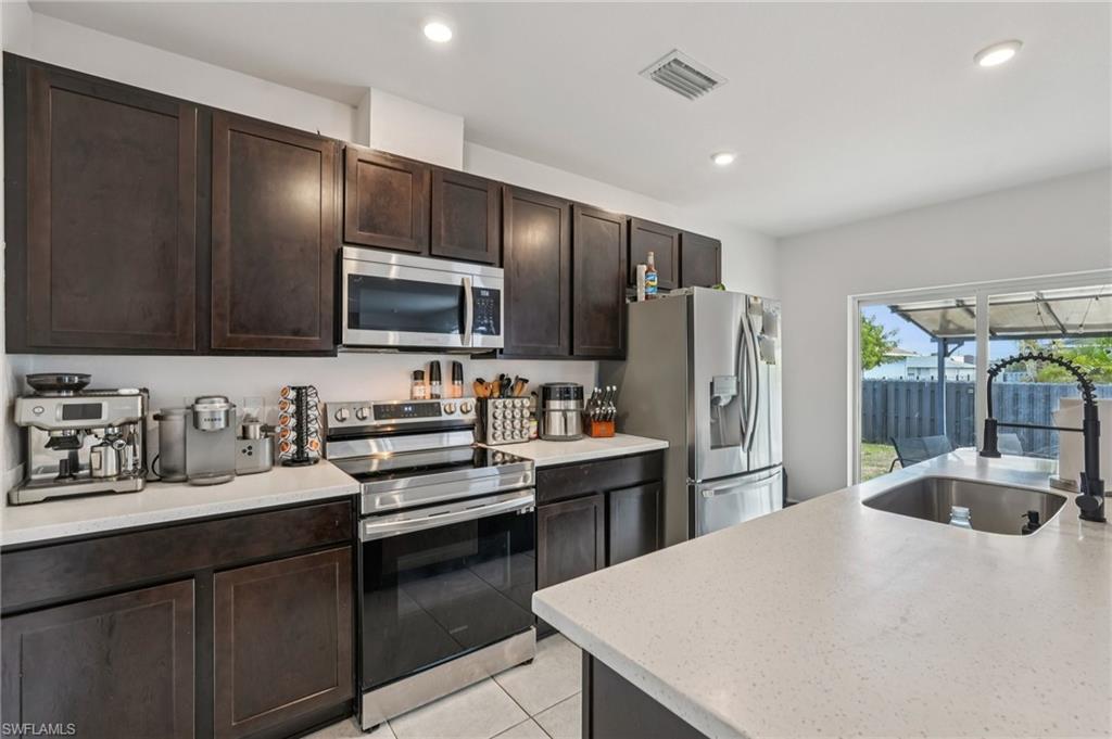 Kitchen with appliances with stainless steel finishes, dark brown cabinets, light stone countertops, light tile patterned floors, and recessed lighting