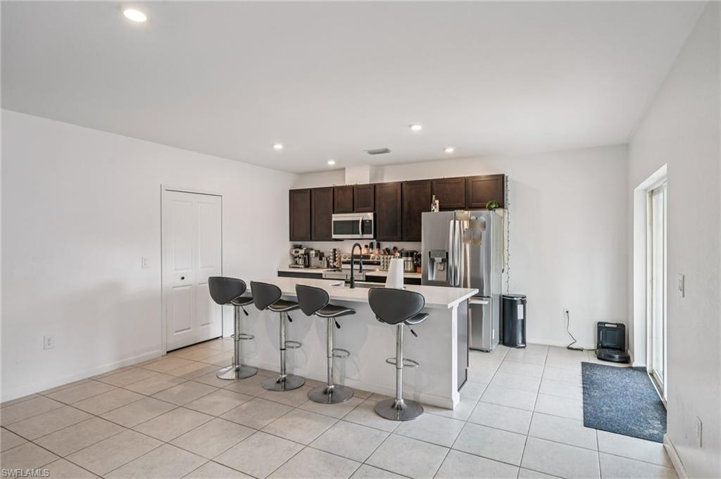 Kitchen featuring dark brown cabinets, a breakfast bar, stainless steel appliances, a kitchen island with sink, and recessed lighting