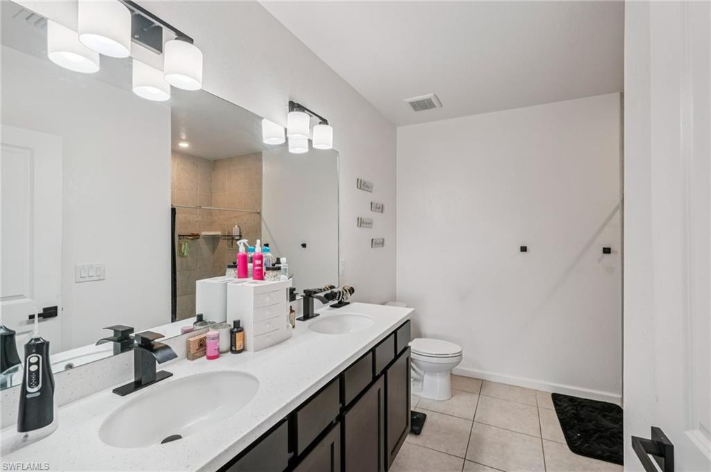 Full bath featuring double vanity, light tile patterned flooring, and a shower stall