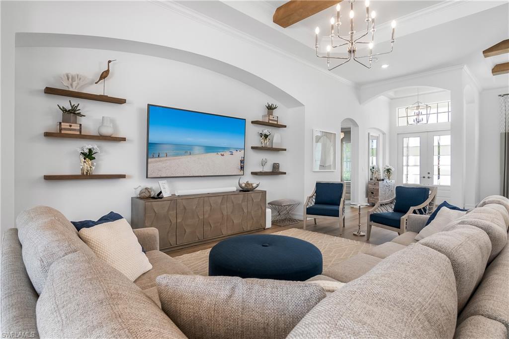 Living area featuring arched walkways, french doors, wood finished floors, ornamental molding, and a chandelier
