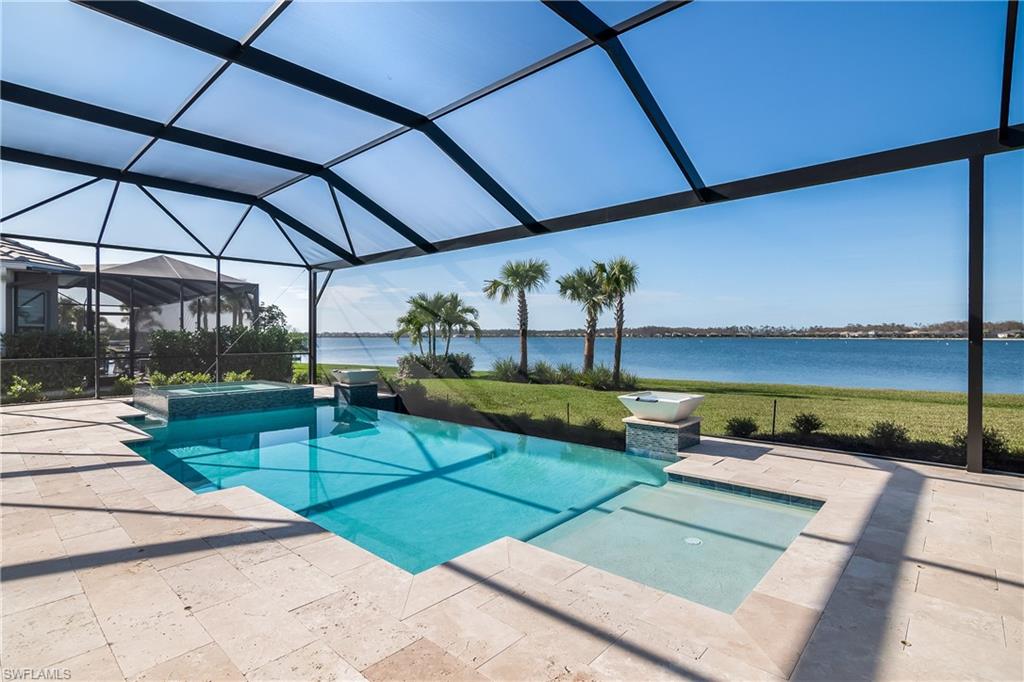 View of pool featuring a water view, glass enclosure, a pool with connected hot tub, and a patio area
