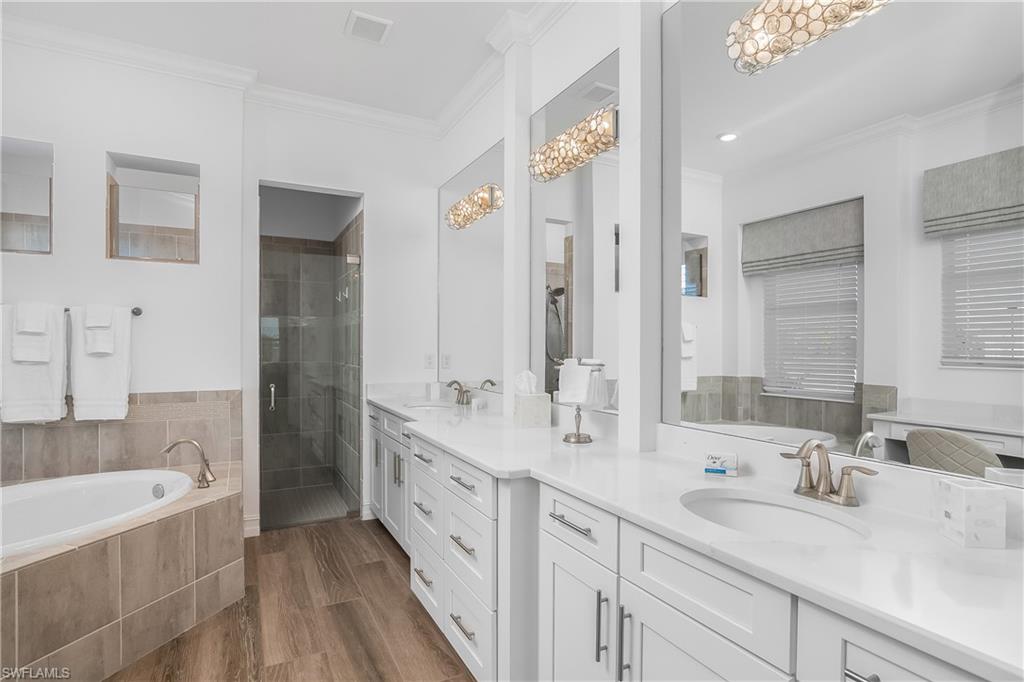 Full bathroom with ornamental molding, double vanity, a garden tub, a stall shower, and dark wood finished floors