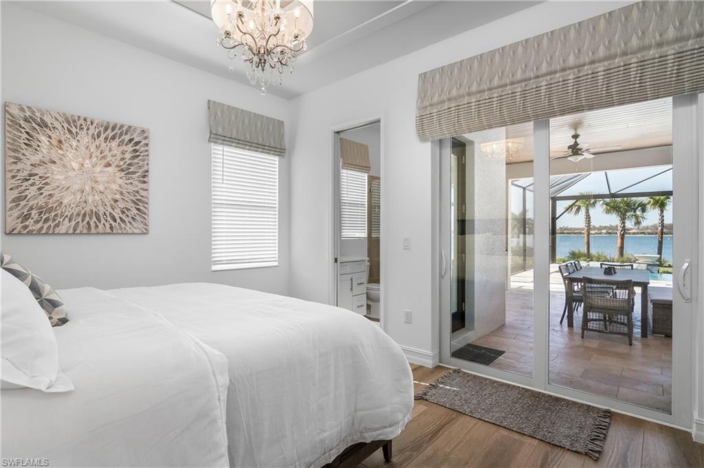 Bedroom with a sunroom, wood finished floors, a water view, access to outside, and a chandelier