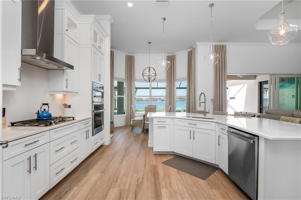 Kitchen featuring white cabinetry, wall chimney exhaust hood, pendant lighting, stainless steel appliances, and crown molding