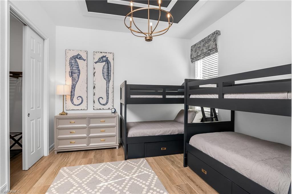 Bedroom with a tray ceiling, light wood-style flooring, a chandelier, and a closet