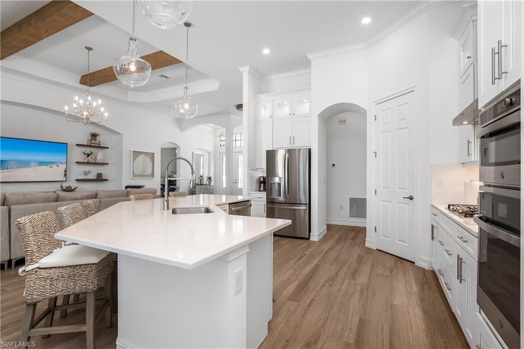 Kitchen with open floor plan, appliances with stainless steel finishes, white cabinetry, arched walkways, and glass insert cabinets