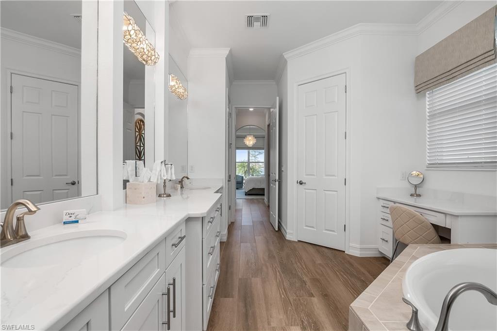 Full bath featuring double vanity, a relaxing tiled tub, crown molding, dark wood-style flooring, and connected bathroom