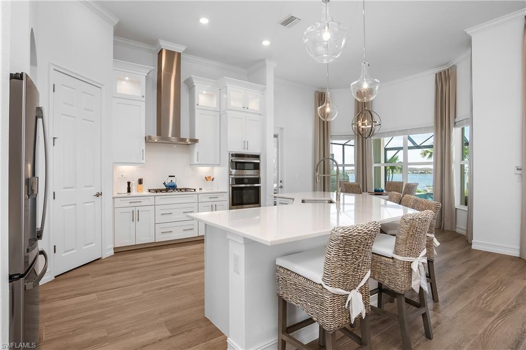 Kitchen featuring glass insert cabinets, crown molding, pendant lighting, a kitchen breakfast bar, and white cabinets