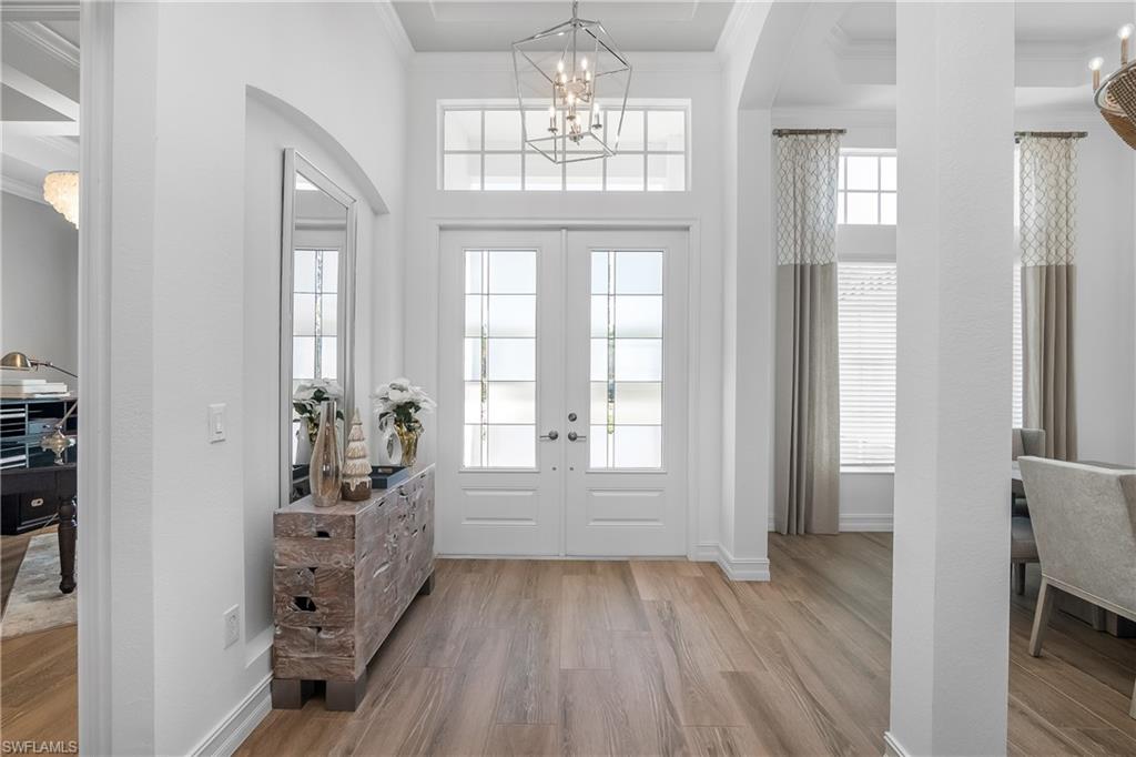 Foyer with a chandelier, crown molding, light wood finished floors, arched walkways, and plenty of natural light
