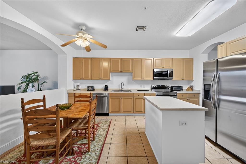 Kitchen featuring New stainless steel Stove, Microwave, dishwasher, arched walkways, light countertops, and light tile patterned floors