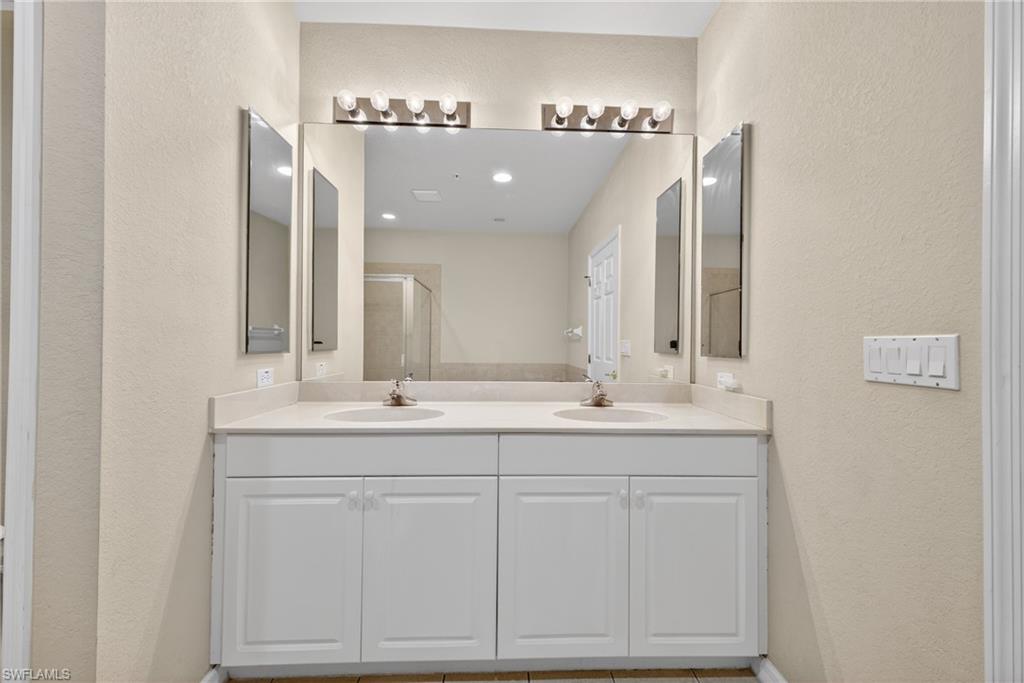 Bathroom featuring a textured wall, double vanity, and a shower stall