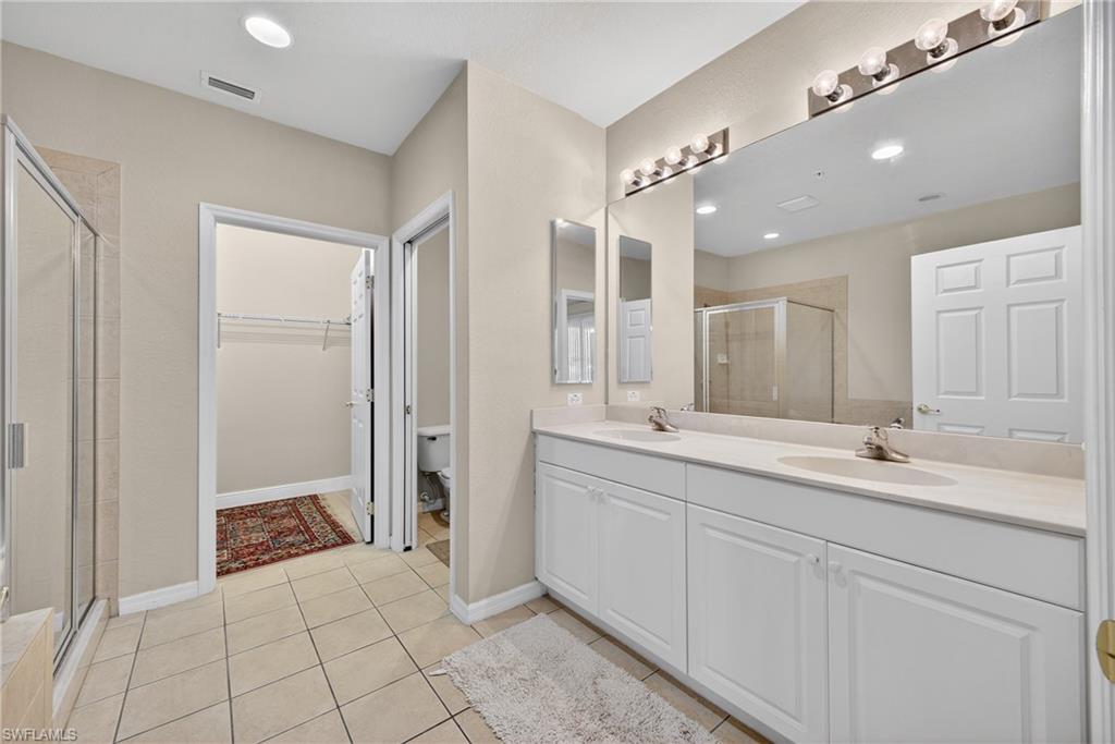 Bathroom with a spacious closet, a shower stall, double vanity, light tile patterned flooring, and recessed lighting