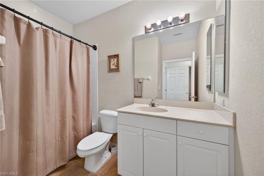 Bathroom with a textured wall, vanity, shower / bath combination with curtain, and light tile patterned floors