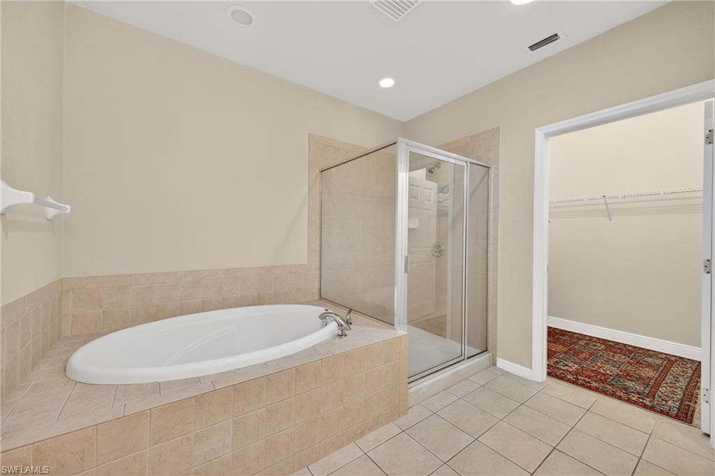 Bathroom featuring a spacious closet, a bath, light tile patterned flooring, a shower stall, and recessed lighting