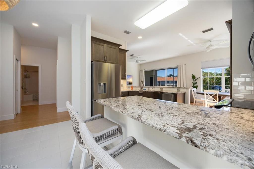 Kitchen featuring appliances with stainless steel finishes, light stone counters, kitchen peninsula, a breakfast bar area, and ceiling fan