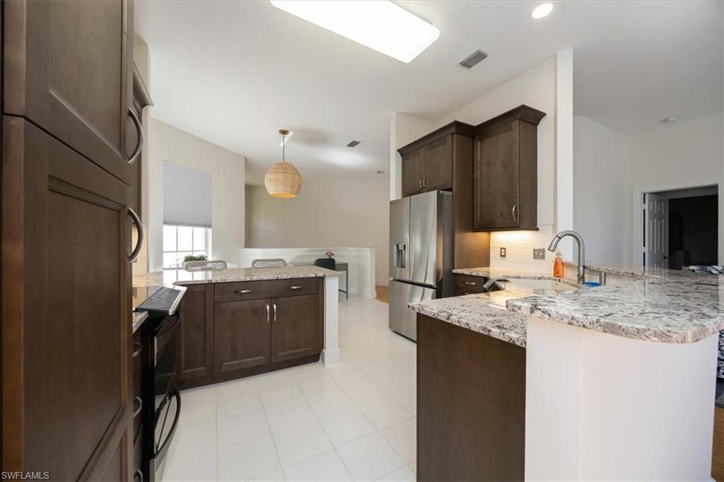 Kitchen with sink, stainless steel refrigerator with ice dispenser, kitchen peninsula, dark brown cabinetry, and light stone countertops
