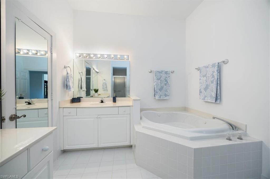 Bathroom featuring tiled tub, vanity, and tile patterned flooring