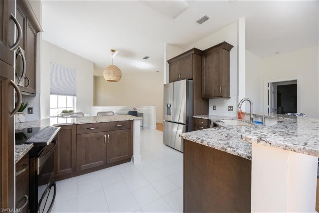 Kitchen featuring dark brown cabinets, light stone counters, stainless steel fridge with ice dispenser, sink, and kitchen peninsula