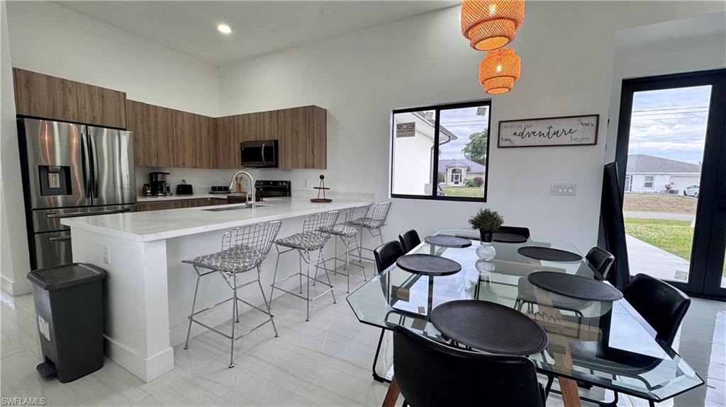Kitchen featuring brown cabinetry, stainless steel appliances, a kitchen bar, modern cabinets, and hanging light fixtures