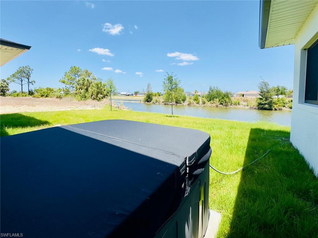 View of green lawn featuring a water view, a hot tub, and a patio area