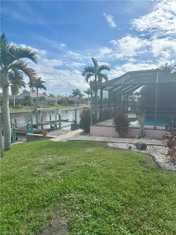 Dock area with boat lift, a lawn, glass enclosure, a water view, and an outdoor pool