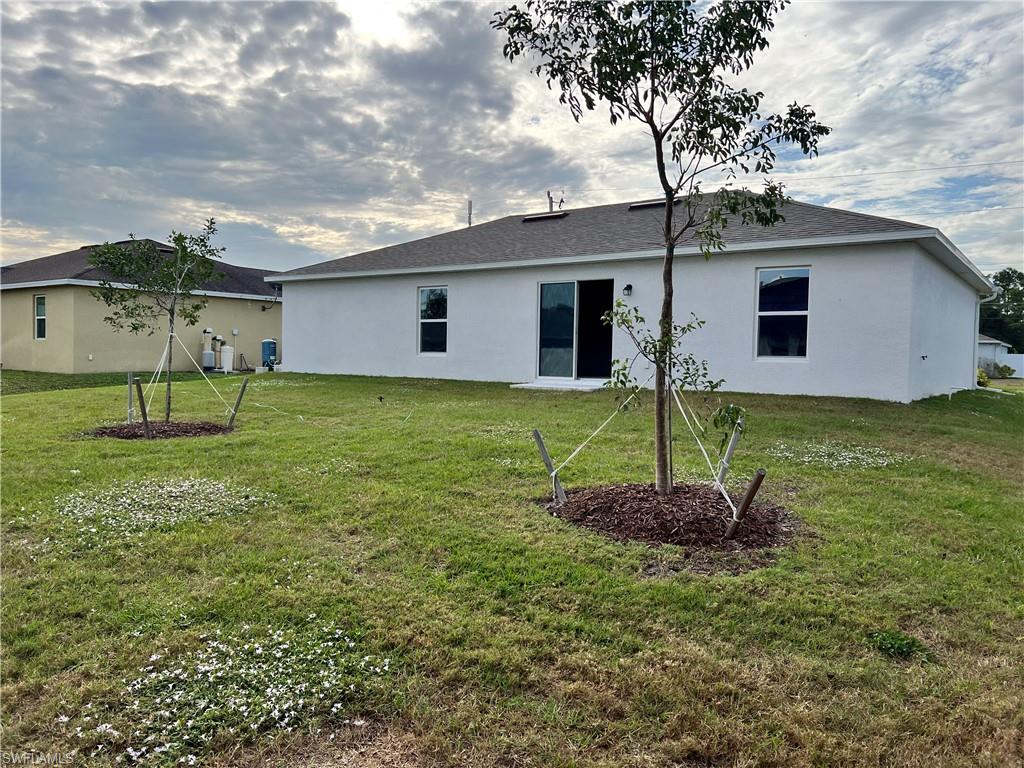 Rear view of property featuring stucco siding, a lawn, and roof with shingles