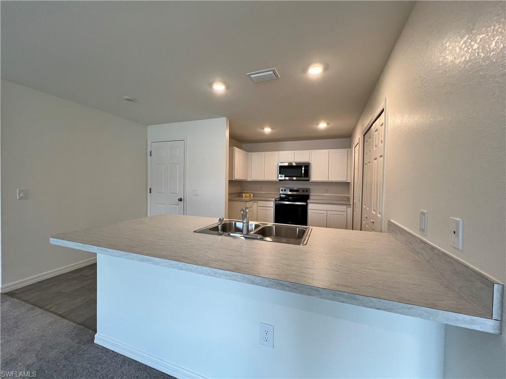Kitchen featuring a peninsula, white cabinetry, light countertops, electric stove, and stainless steel microwave