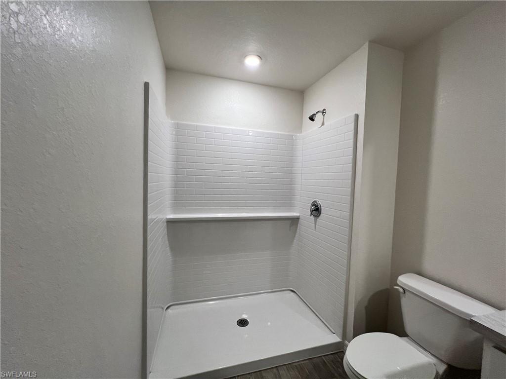 Full bath with a shower stall, a textured wall, and dark wood finished floors