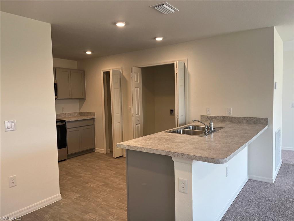 Kitchen with a peninsula, gray cabinets, a kitchen bar, stainless steel range oven, and light countertops