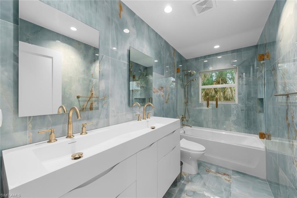 Bathroom with tile walls, double vanity, marble tiled floors, shower / tub combination, and recessed lighting