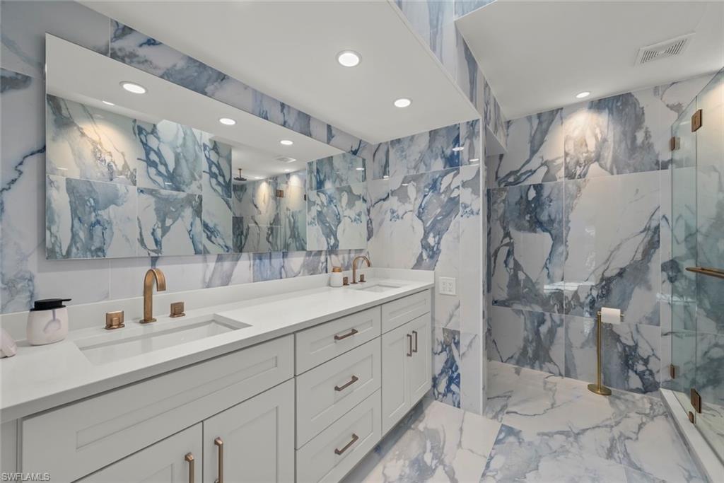 Full bath featuring a marble finish shower, double vanity, stone wall, recessed lighting, and light marble finish flooring