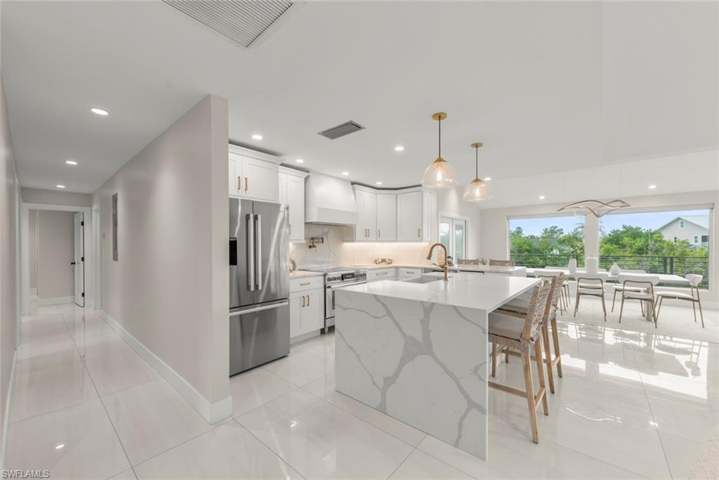 Kitchen featuring appliances with stainless steel finishes, light stone counters, pendant lighting, white cabinets, and premium range hood
