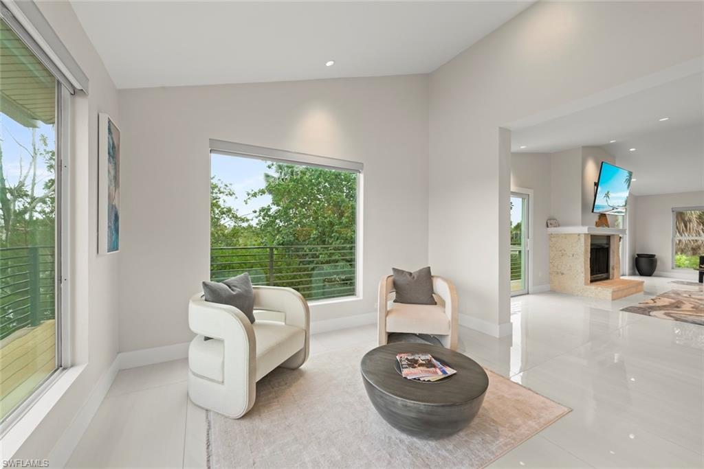 Sitting room featuring vaulted ceiling, plenty of natural light, a fireplace with raised hearth, tile patterned floors, and recessed lighting