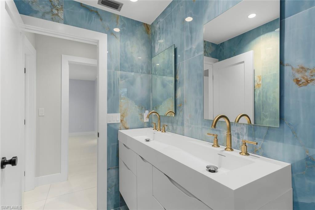 Bathroom featuring tile walls, double vanity, and light tile patterned floors