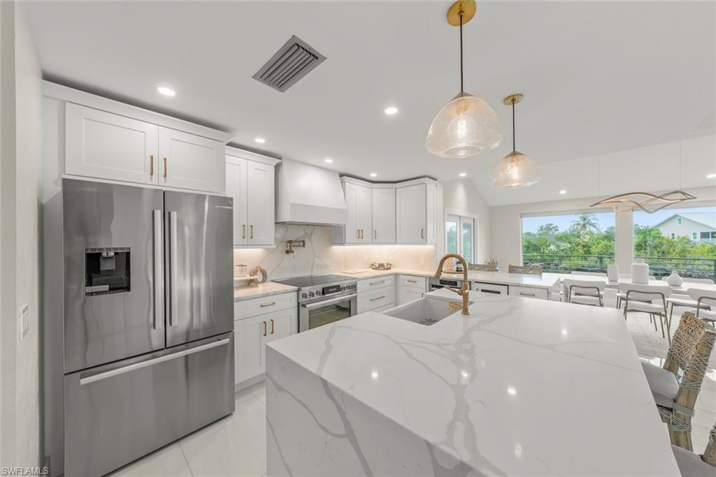 Kitchen featuring appliances with stainless steel finishes, white cabinetry, light stone countertops, vaulted ceiling, and a breakfast bar area