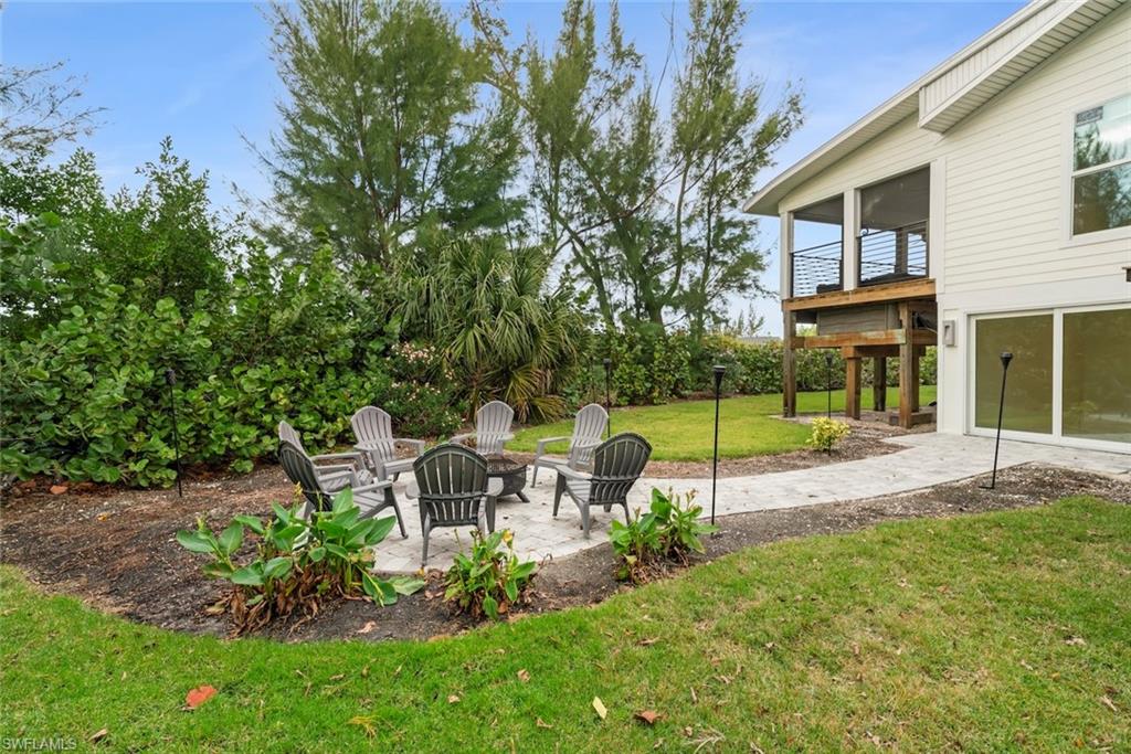 View of grassy yard with a patio area, a sunroom, and a fire pit