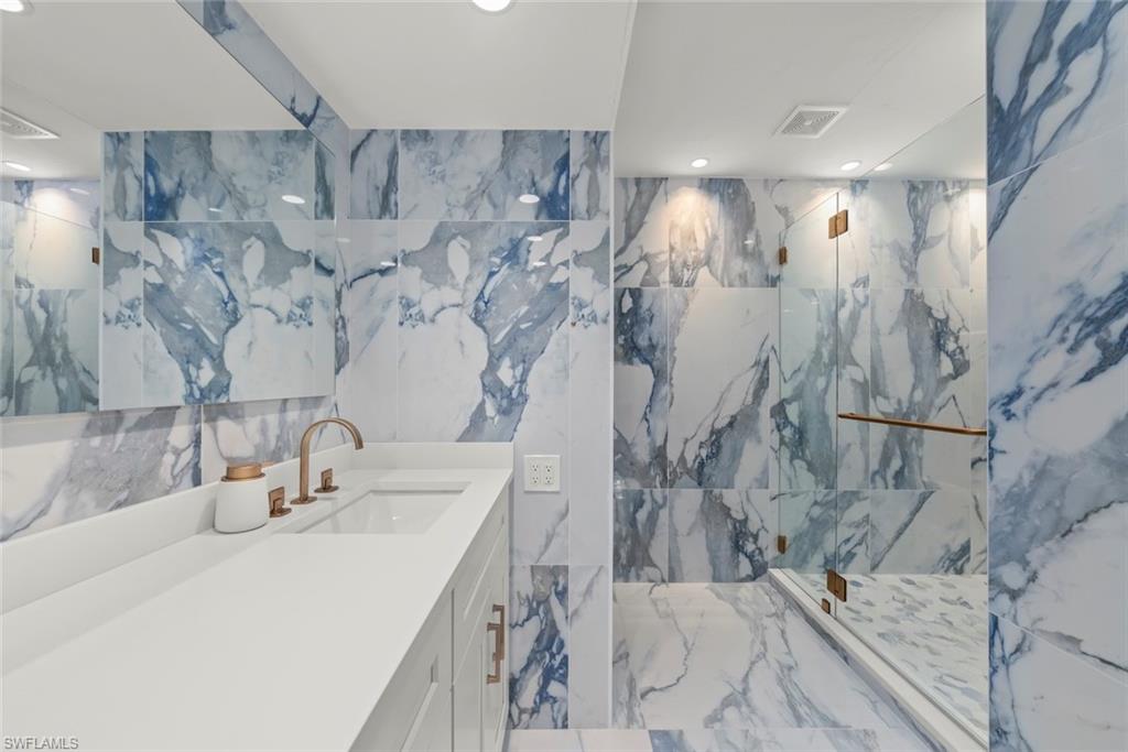 Full bath featuring stone wall, a marble finish shower, vanity, marble tiled flooring, and tile walls