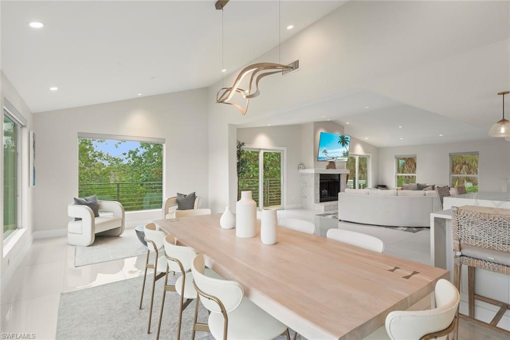 Dining room featuring a fireplace, light tile patterned floors, healthy amount of natural light, recessed lighting, and high vaulted ceiling