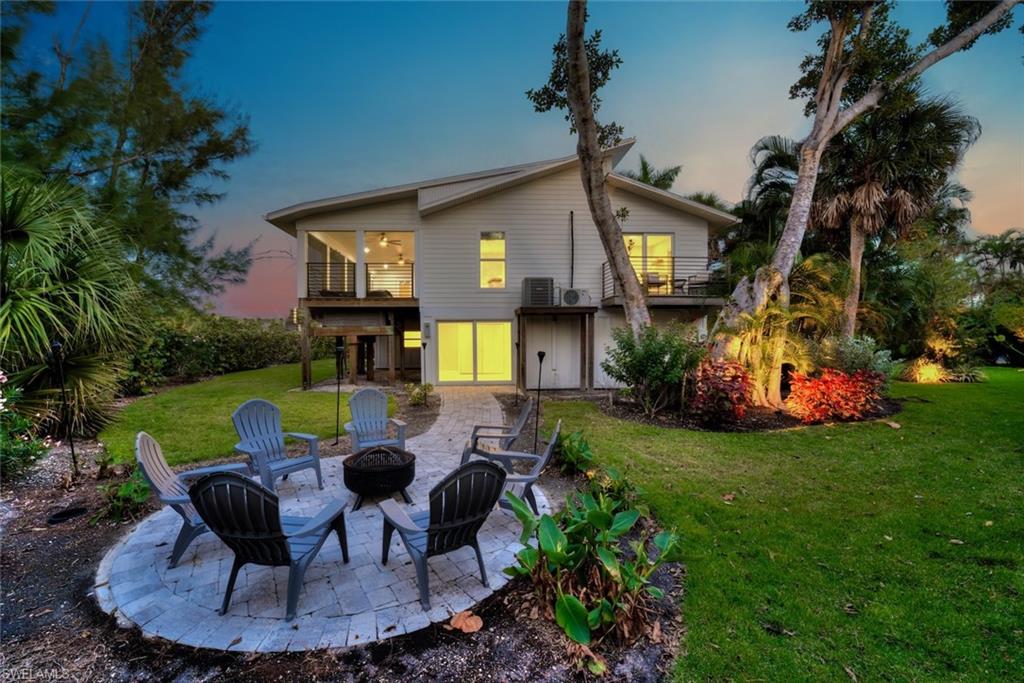 Back of house at dusk featuring a patio area, a lawn, a balcony, and a fire pit