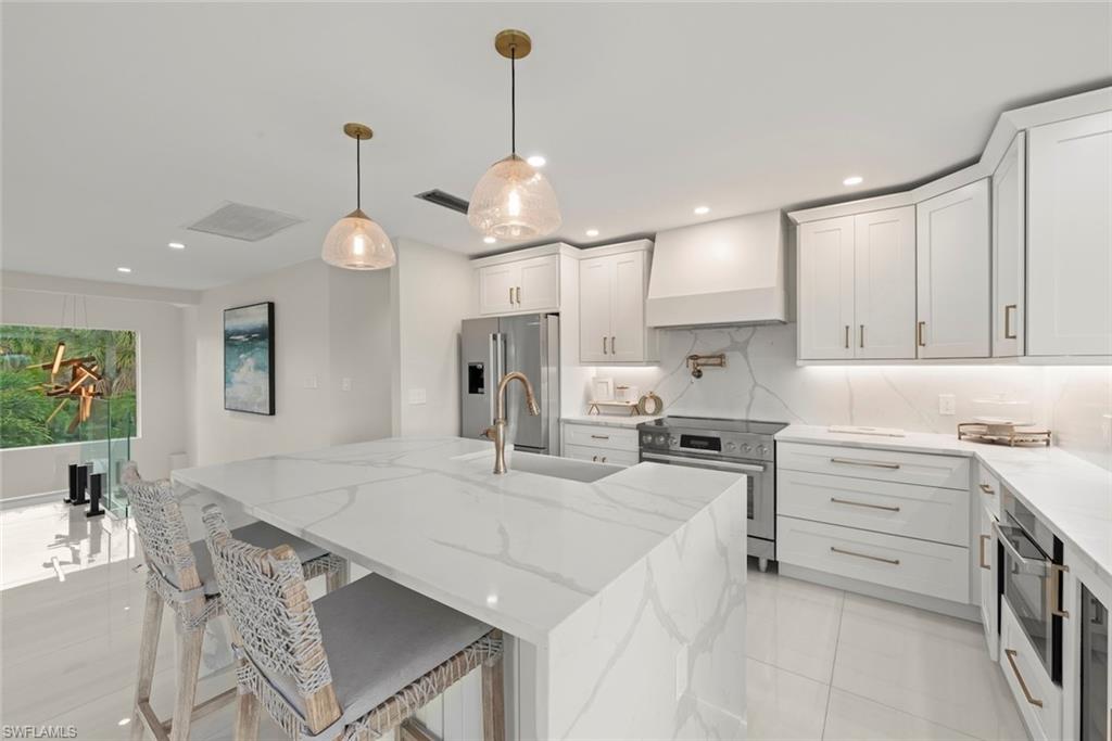 Kitchen featuring light stone counters, hanging light fixtures, appliances with stainless steel finishes, an island with sink, and custom range hood
