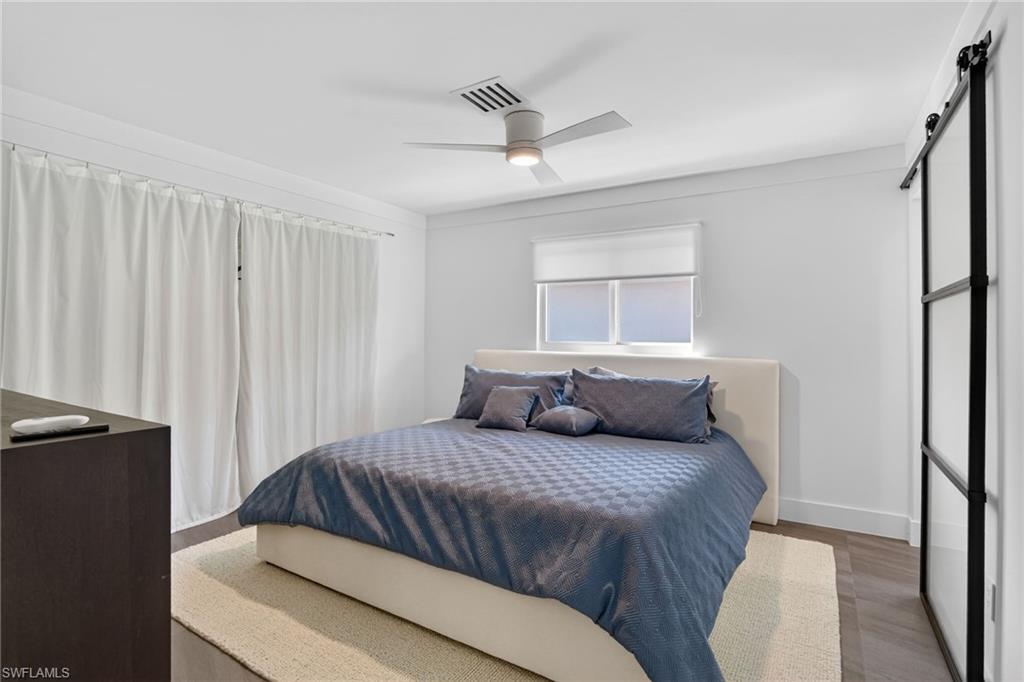 Bedroom with a barn door, wood finished floors, and a ceiling fan