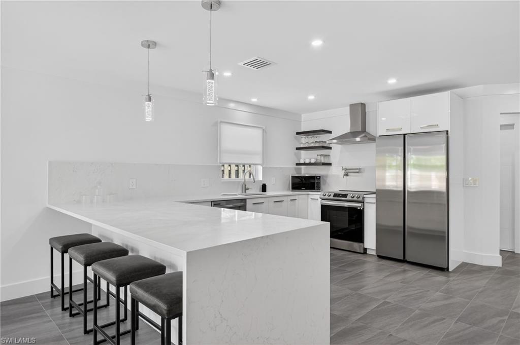 Kitchen featuring open shelves, a breakfast bar area, appliances with stainless steel finishes, decorative backsplash, and white cabinetry