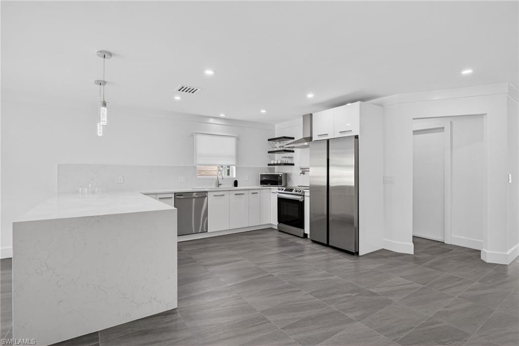 Kitchen featuring stainless steel appliances, decorative light fixtures, white cabinetry, light stone countertops, and recessed lighting