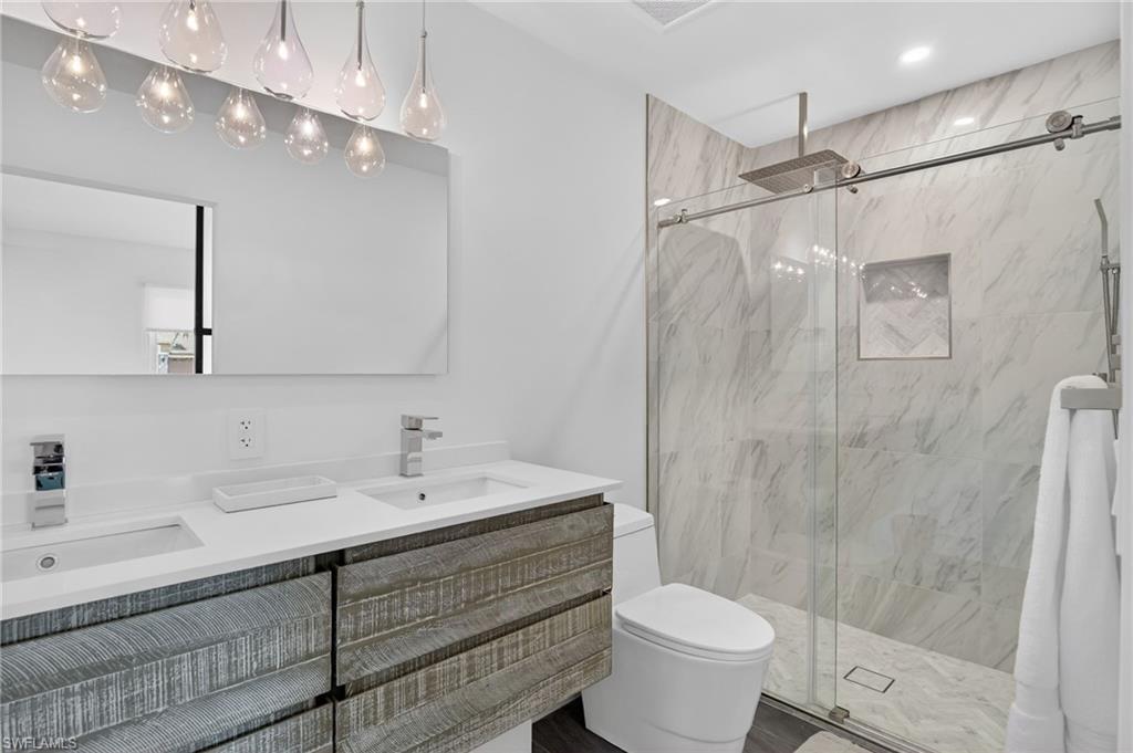 Full bath with double vanity and a marble finish shower