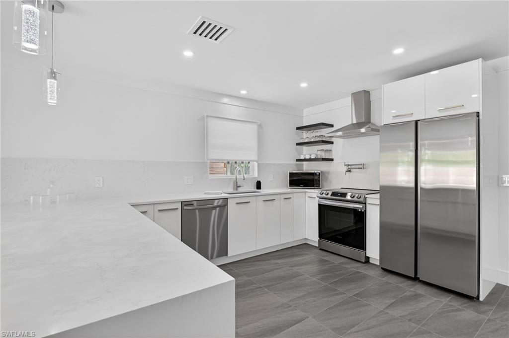Kitchen featuring open shelves, stainless steel appliances, white cabinetry, wall chimney range hood, and light stone counters